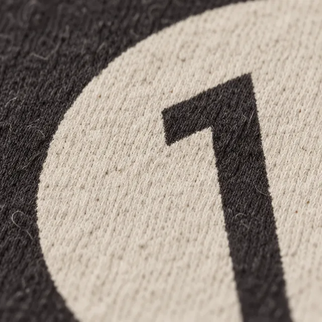 Close on the cream disc on washed black jersey, the 1 inside it left in the shirt’s own black.