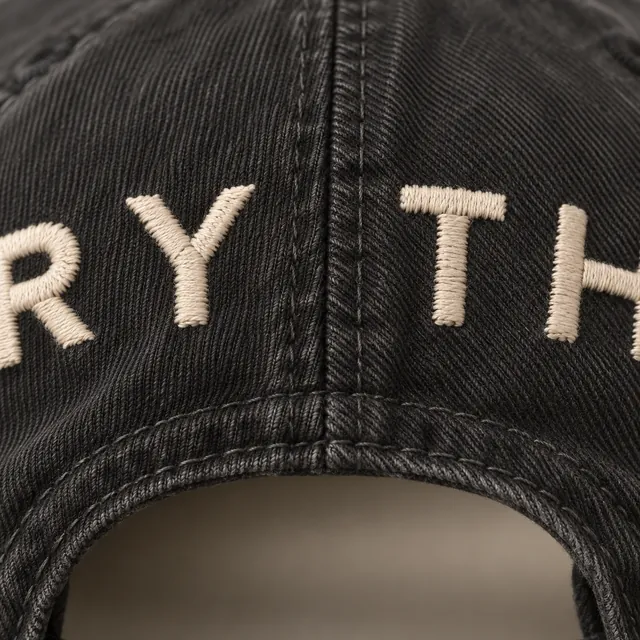 The back of a washed black cap: small cream letters stitched flat above the strap opening.