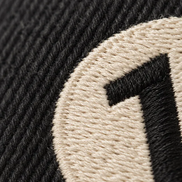 Flat cream satin stitches forming a disc on black twill, a black 1 inside it.