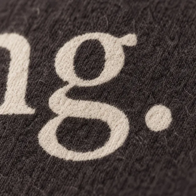 The end of a line of cream serif lettering, its full stop, on black fleece.