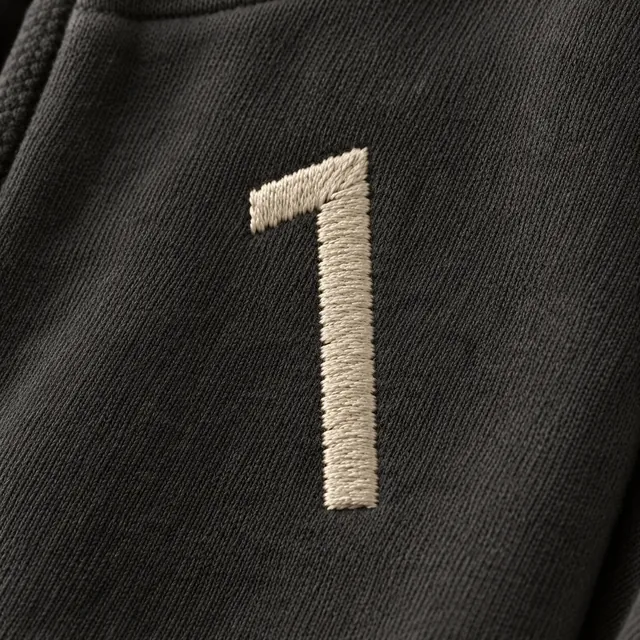 Close on the chest: the 1 in dense cream satin stitch on black fleece.