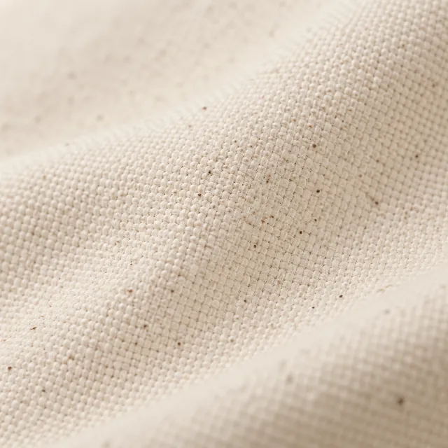 Natural cotton canvas, softly folded, small dark flecks in the cream weave.