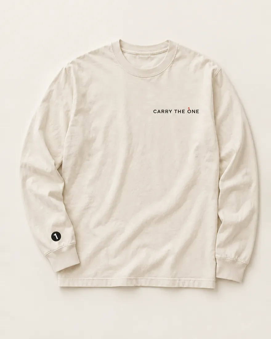 An ecru long sleeve laid flat, Carry the One printed small on the left chest, a small black disc stitched near the cuff.