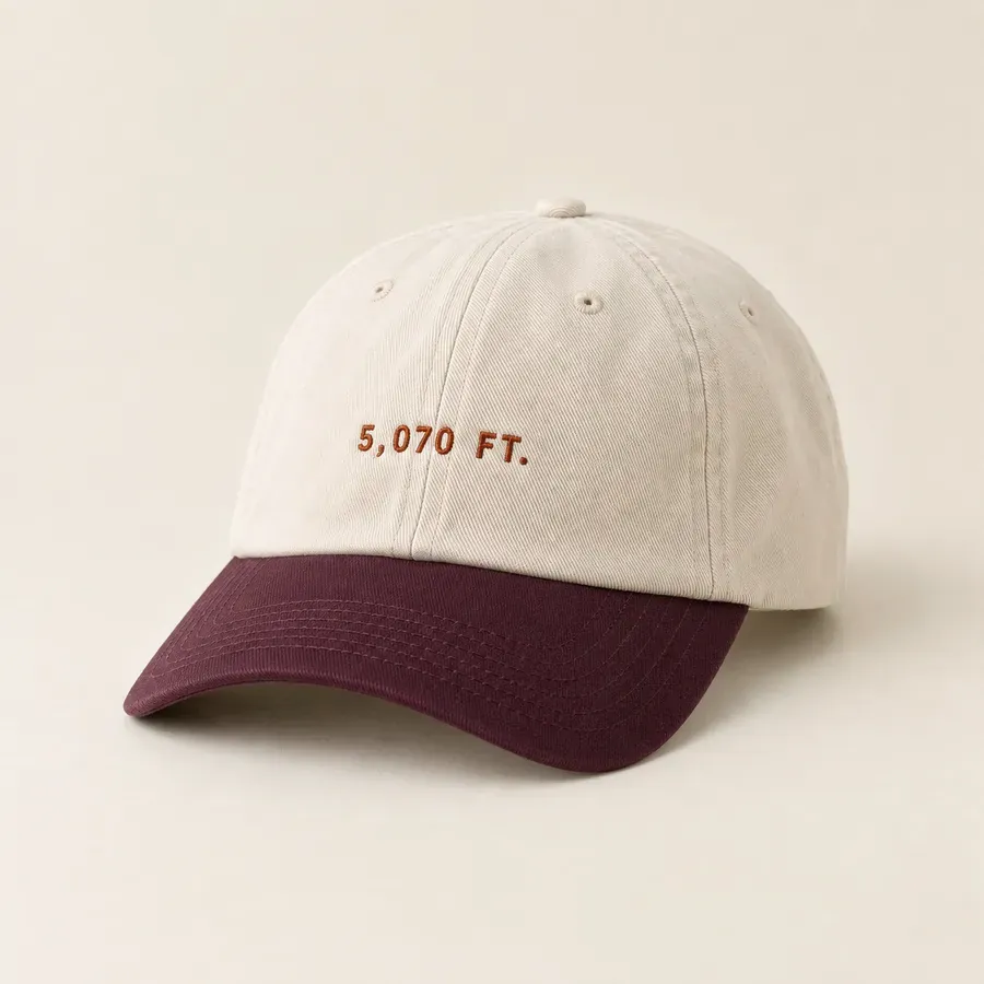 An ecru cotton cap with a plum brim, 5,070 FT. embroidered small across the front in rust thread.