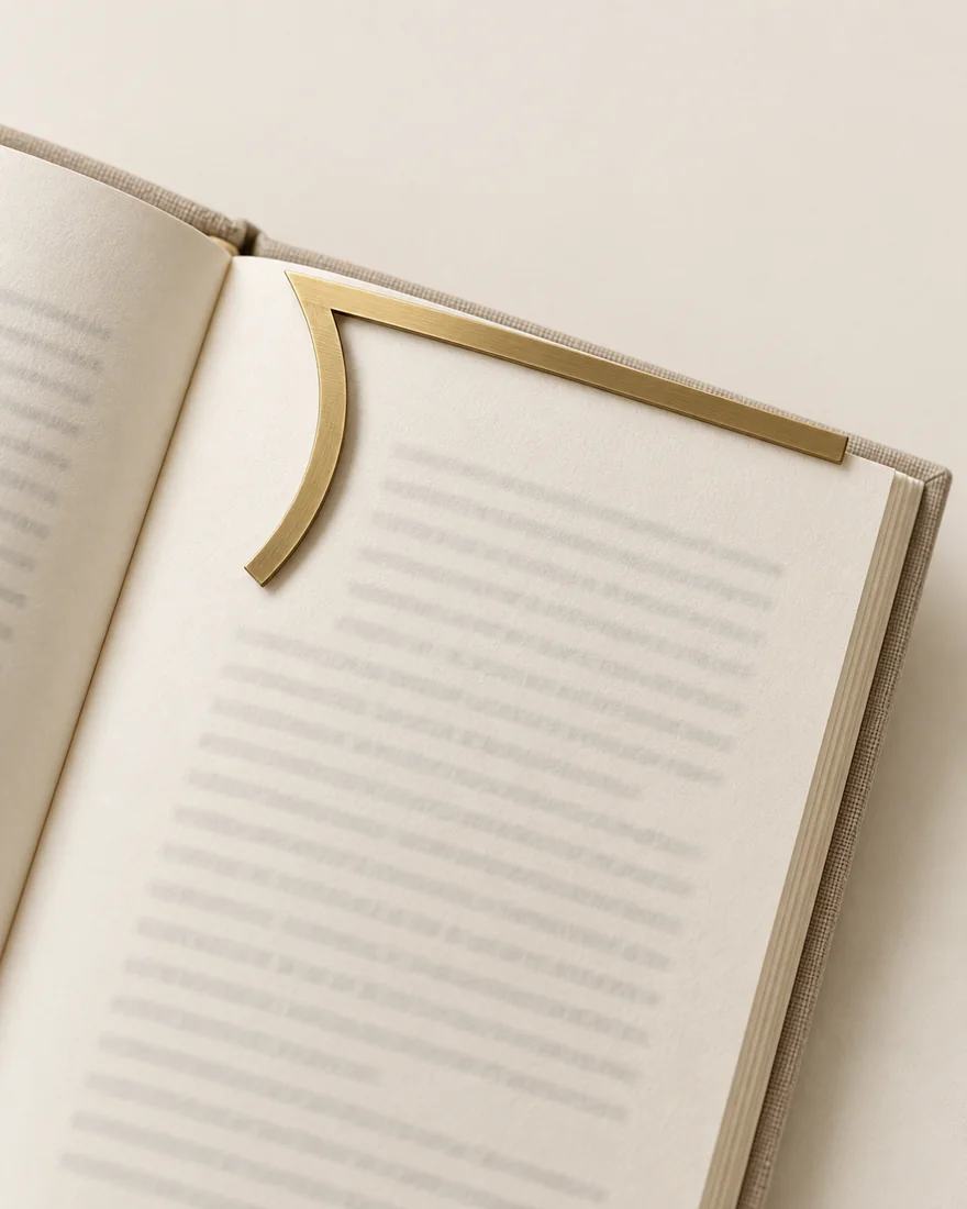 A brushed brass page marker in the shape of the long-division bracket, slipped over the top of an open book’s page.