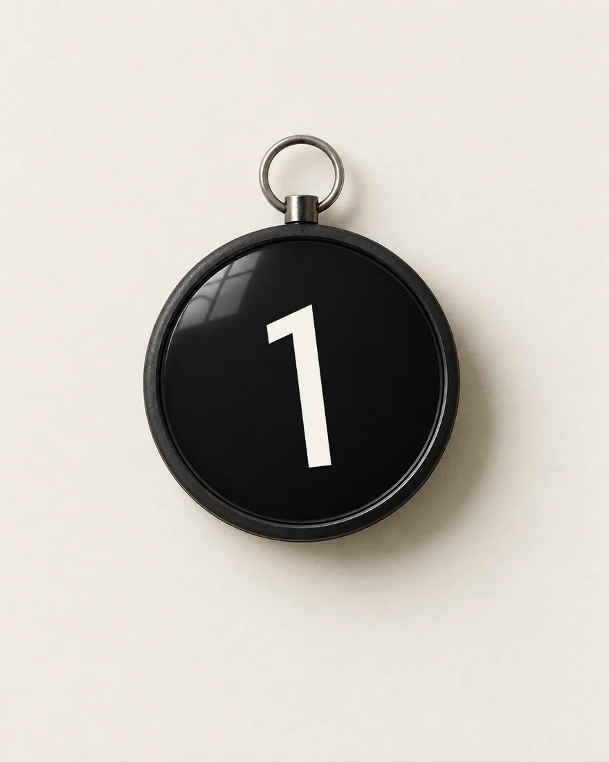 A round black pocket compass whose white needle is cut in the shape of the leaning 1.