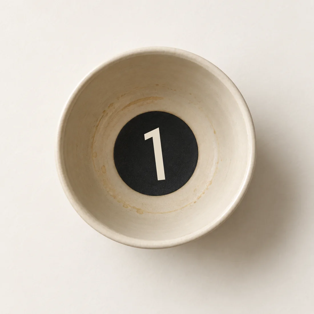 From above: an empty ecru cup with the black disc and its 1 glazed into the bottom of the bowl.